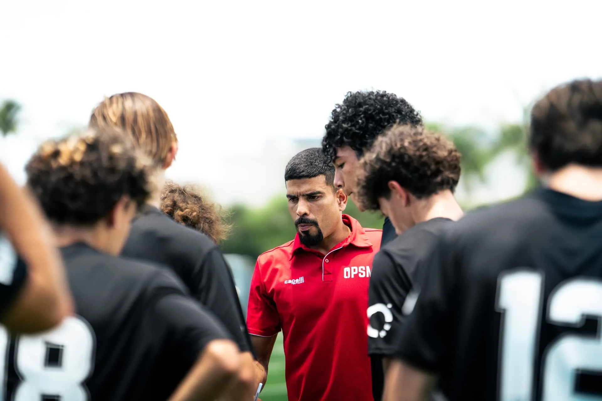 Coach in red OPSM polo addressing players in a huddle